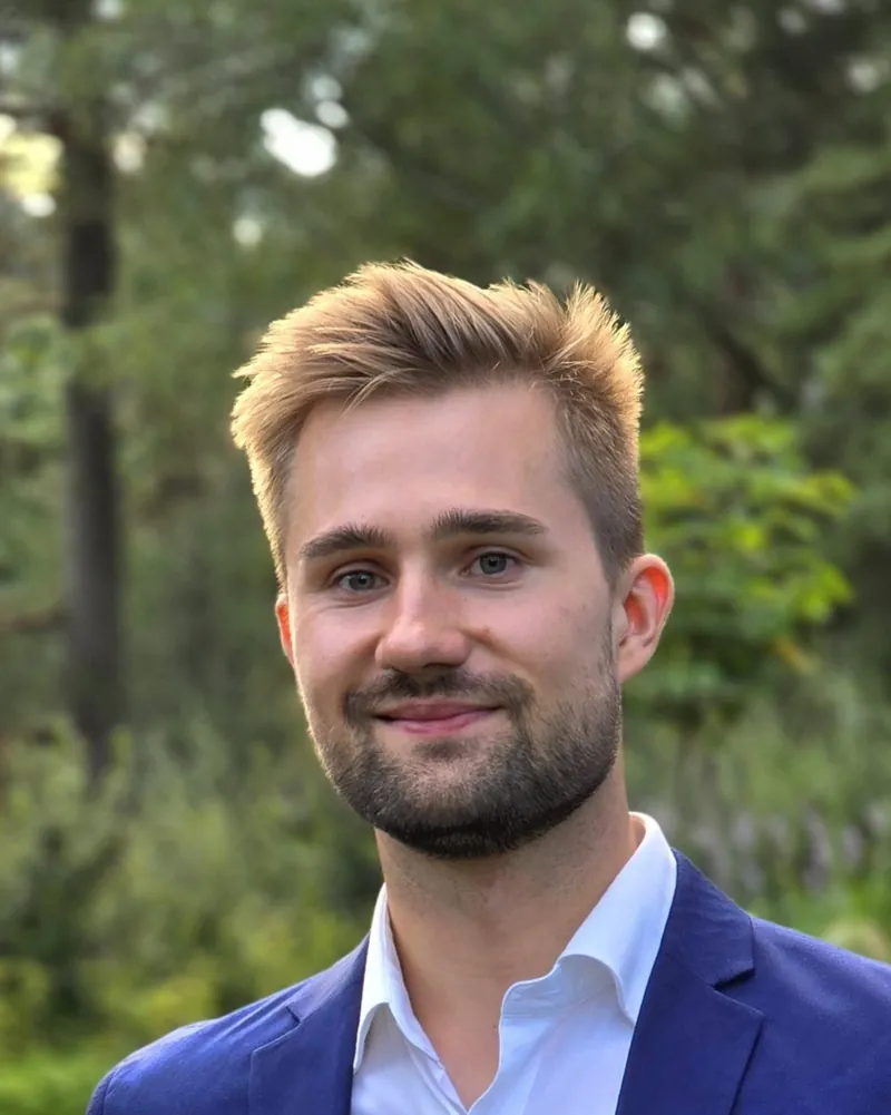 Niko Rantala, smiling in a blue blazer, trees in the background
